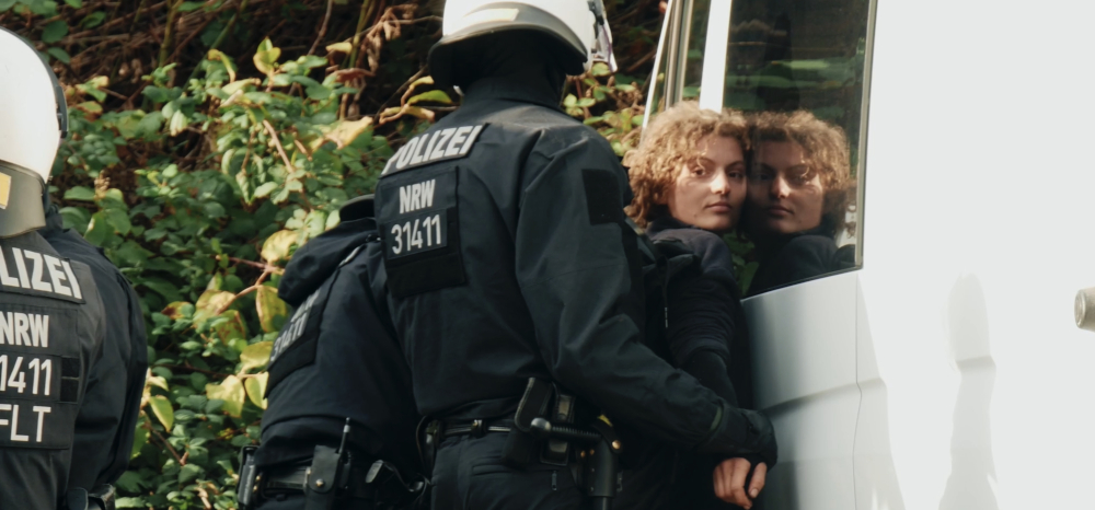 Ein Polizist nimmt eine Frau fest und drückt sie dabei an ein Auto