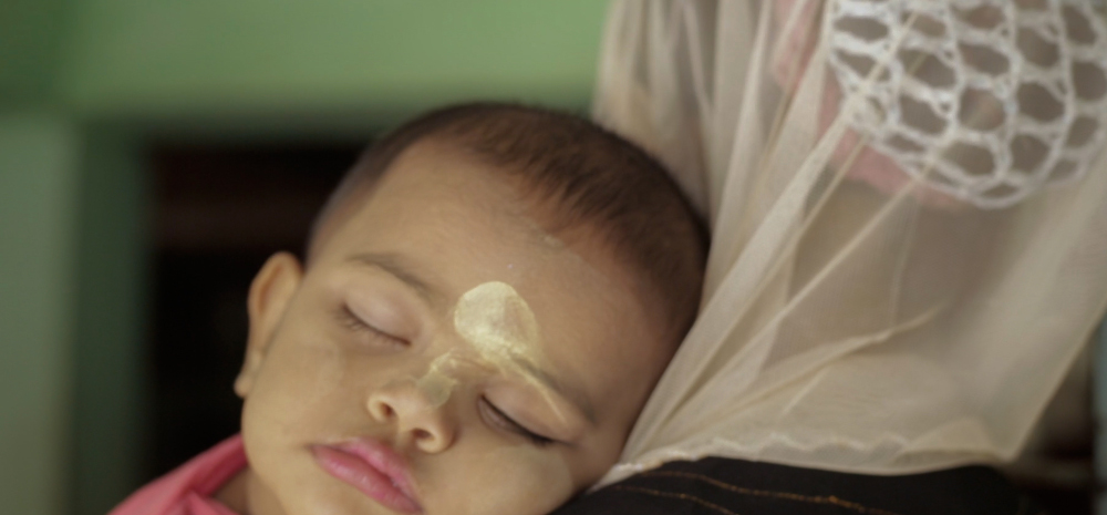ein kleines Kind mit verschmiertem Farbpunkt auf der Stirn hat den Kopf in den Schoß einer Person gelegt und schläft