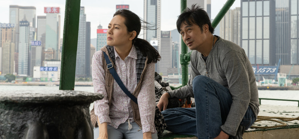 Frau und Mann sitzen in einem Boot, im Hintergrund die Hochhäuser von Hong Kong