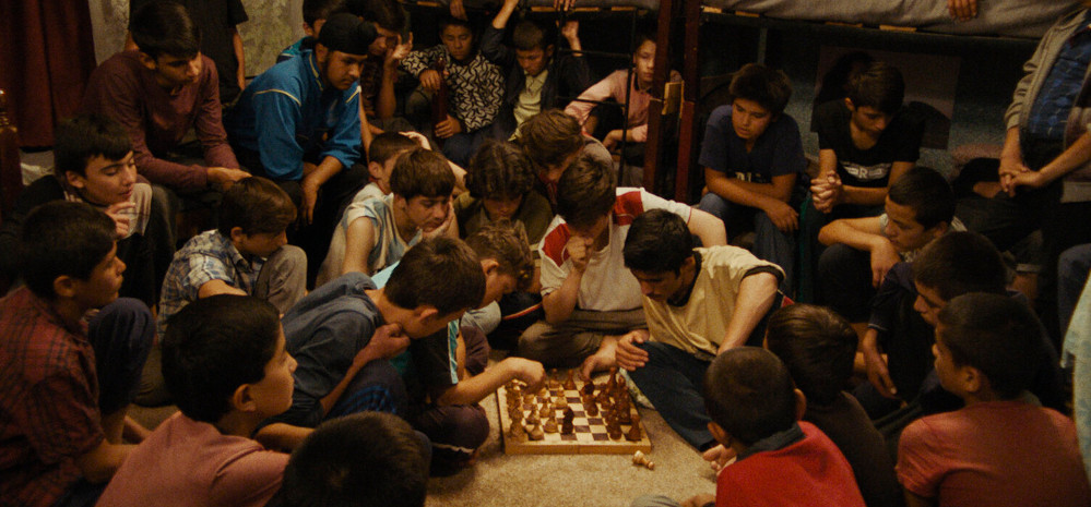 Kinder umringen zwei Jungs, die Schach spielen