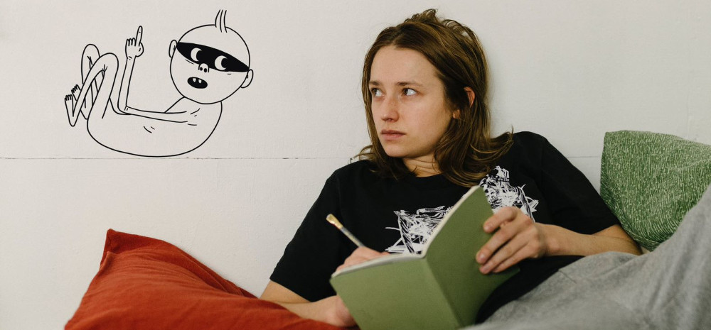 Ein junge Frau im Bett mit Buch in der Hand, an der Wand eine gezeichnete Figur