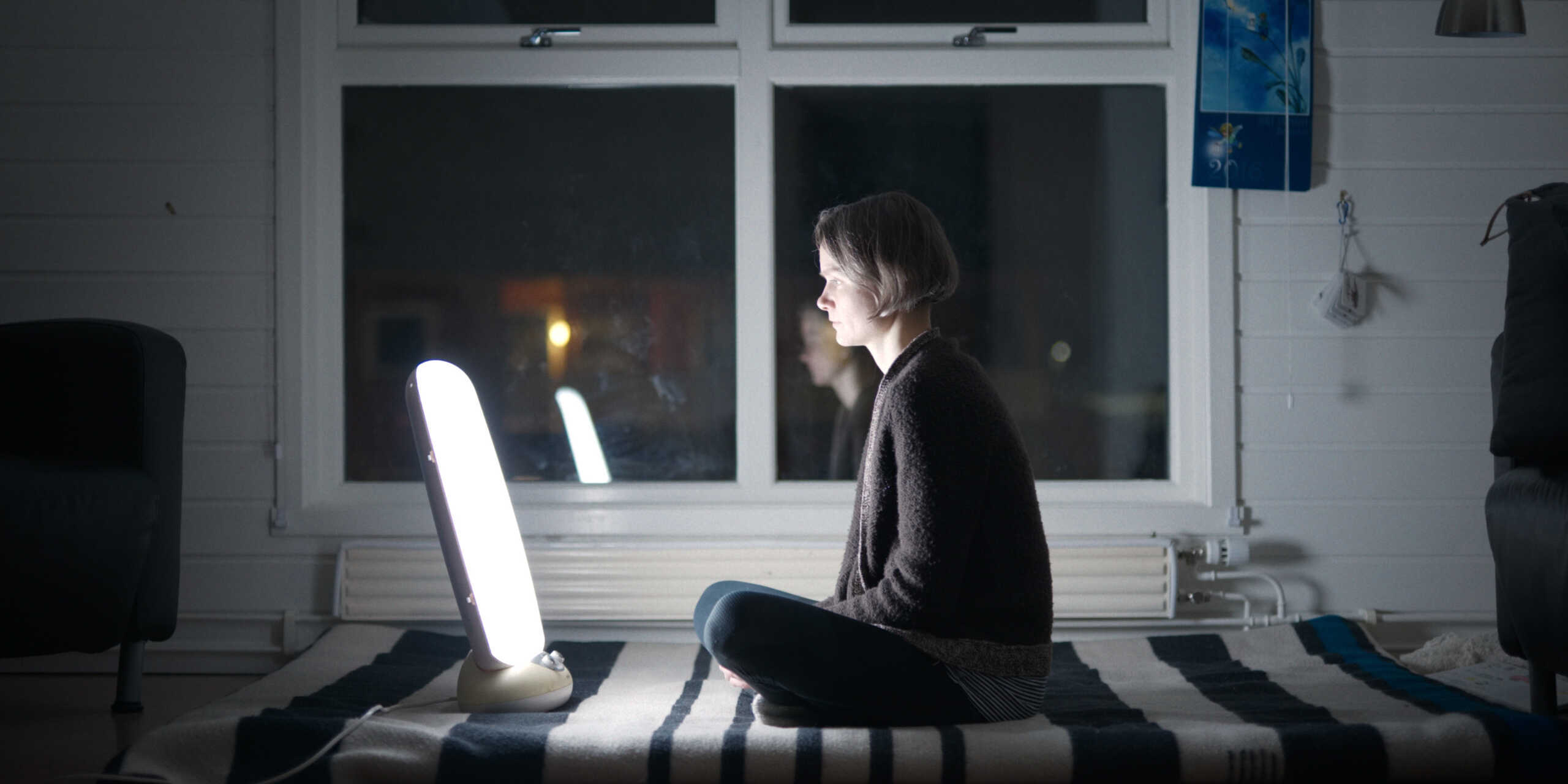 Eine Frau sitzt im Dunkeln vor einer stark leuchtenden Lampe