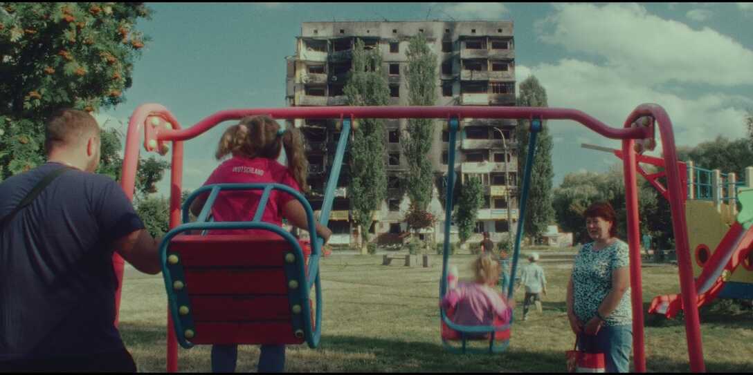 Kinder und Eltern auf einem Kinderspielplatz, im Hintergrund eien Hochhaus