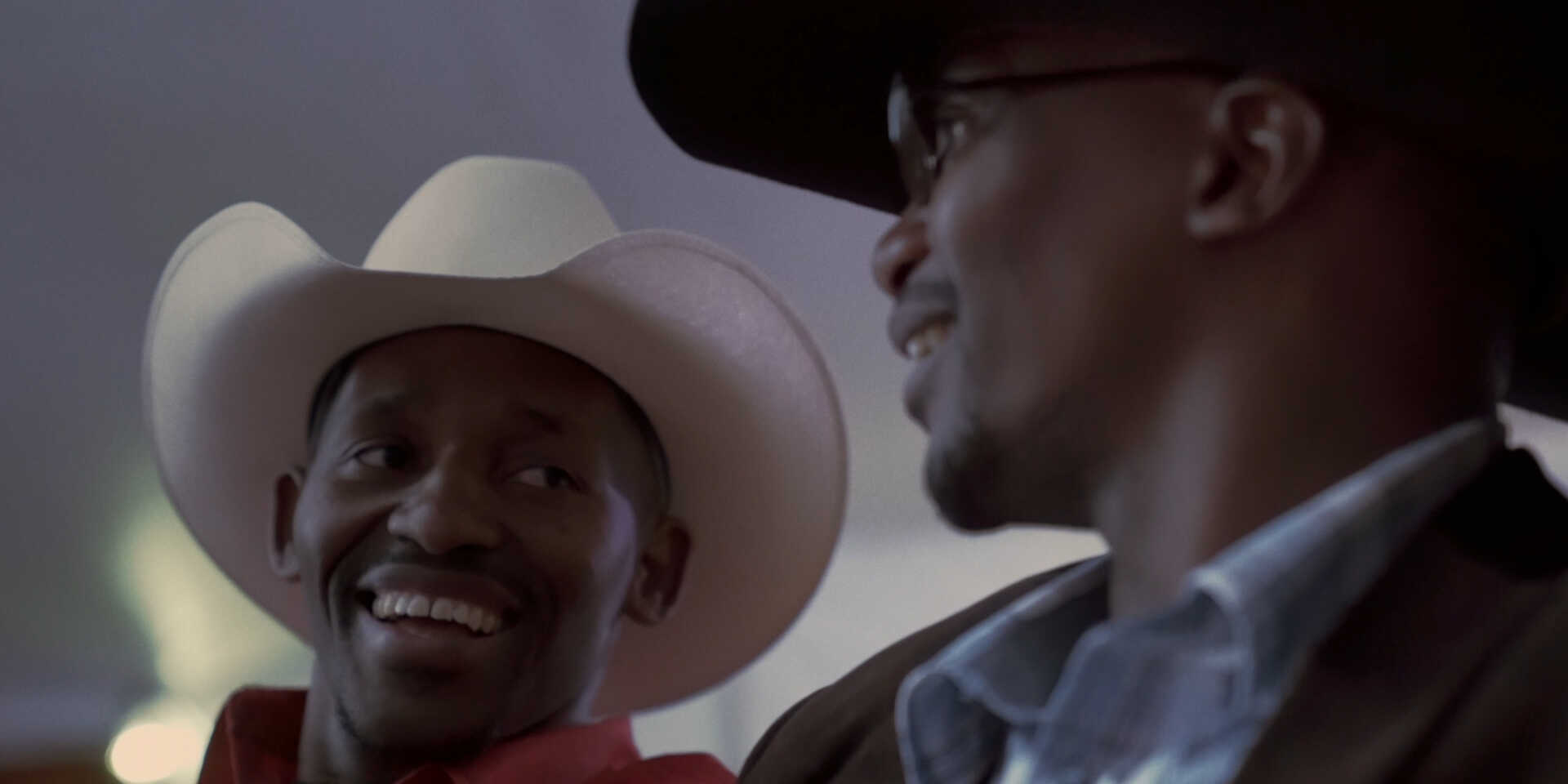 Zwei schwarze Musiker mit Cowboyhut unterhalten sich, nur ihre Köpfe sind zu sehen