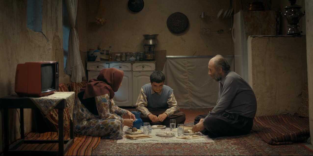 Eine Frau, ein Junge und ein Mann sitzen auf dem Teppichboden beim Essen in ihrem Wohnzimmer