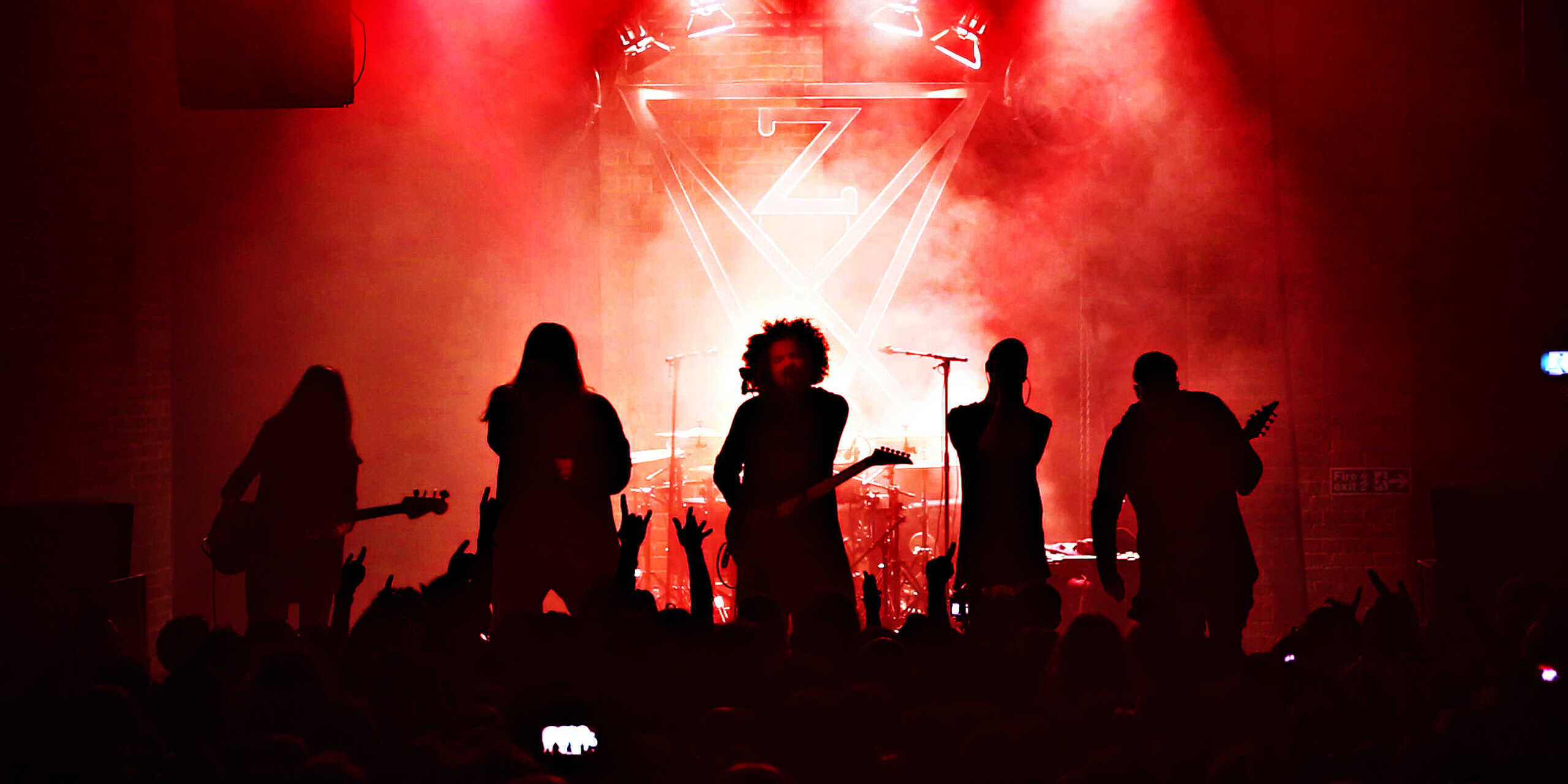 Eine fünfköpfige Metal-Band auf der Bühne, alles ist in rotes Licht getaucht